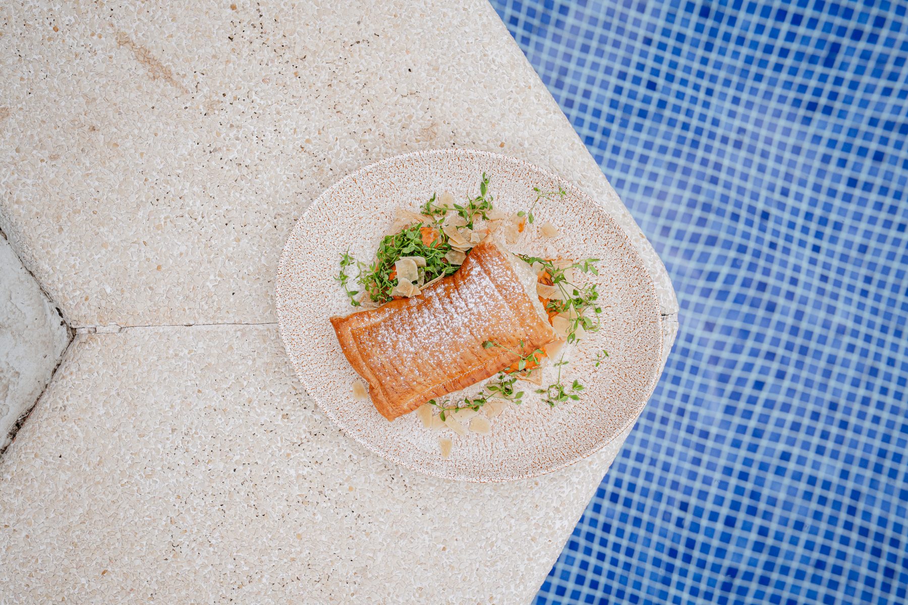 Plato de autor junto a una piscina de mosaico azul